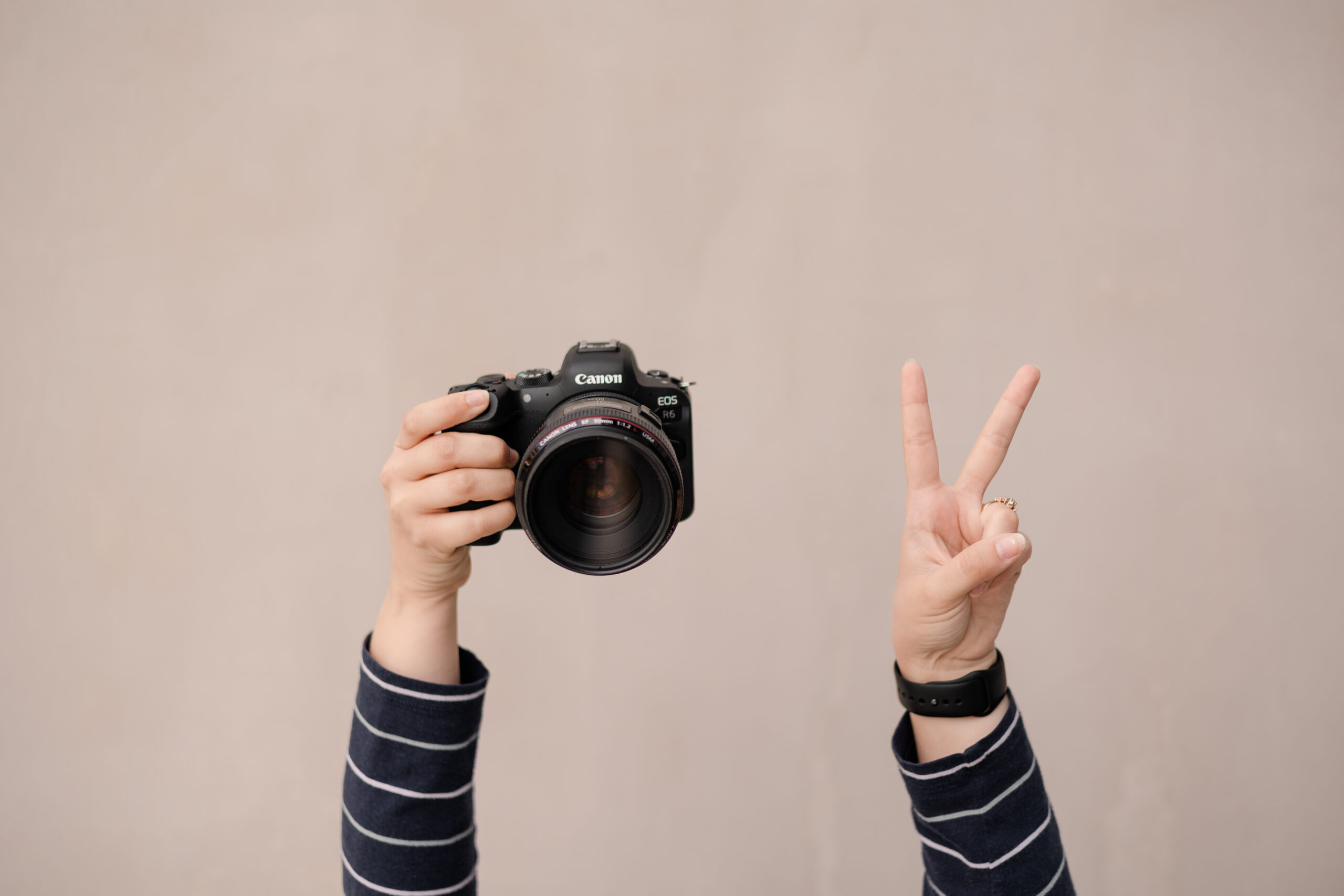 a woman holds a canon camera up in the air while also throwing up a peace sign