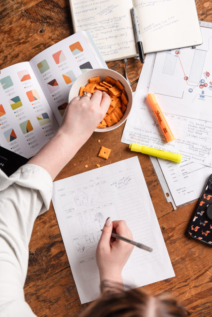a woman works on a storyboard for a video production project, while snacking on cheez-its, her favorite snack