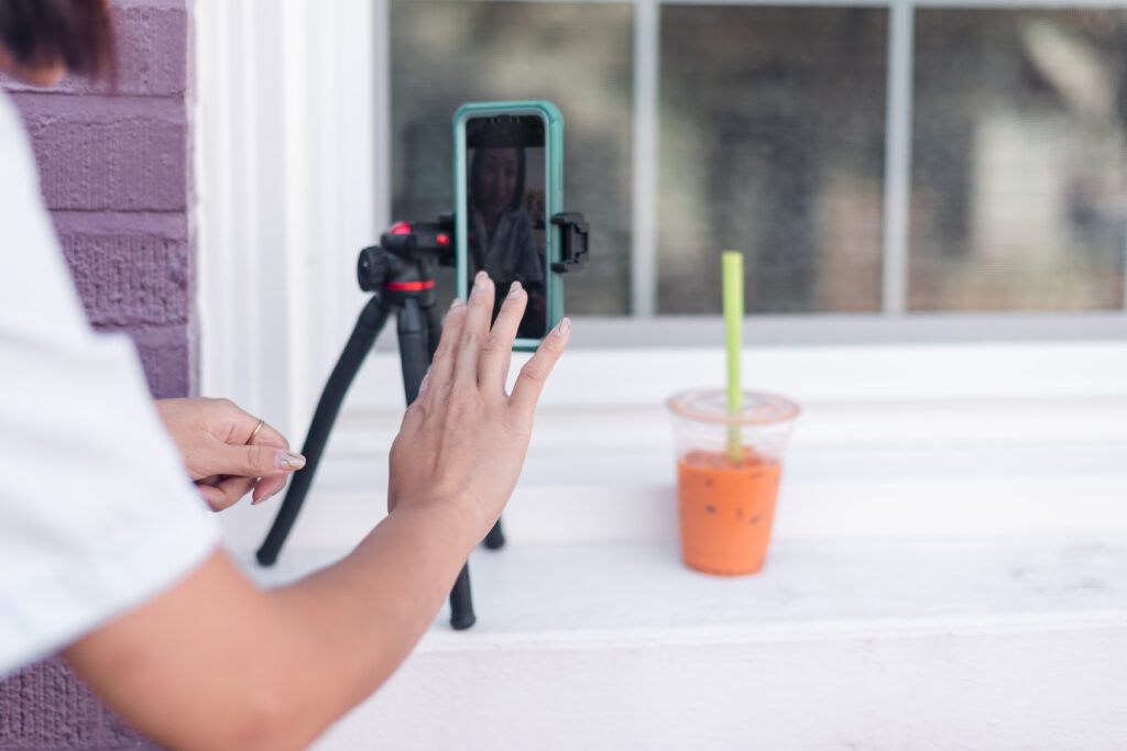 a woman records content on her cell phone, with a cup of boba tea resting nearby for enjoyment