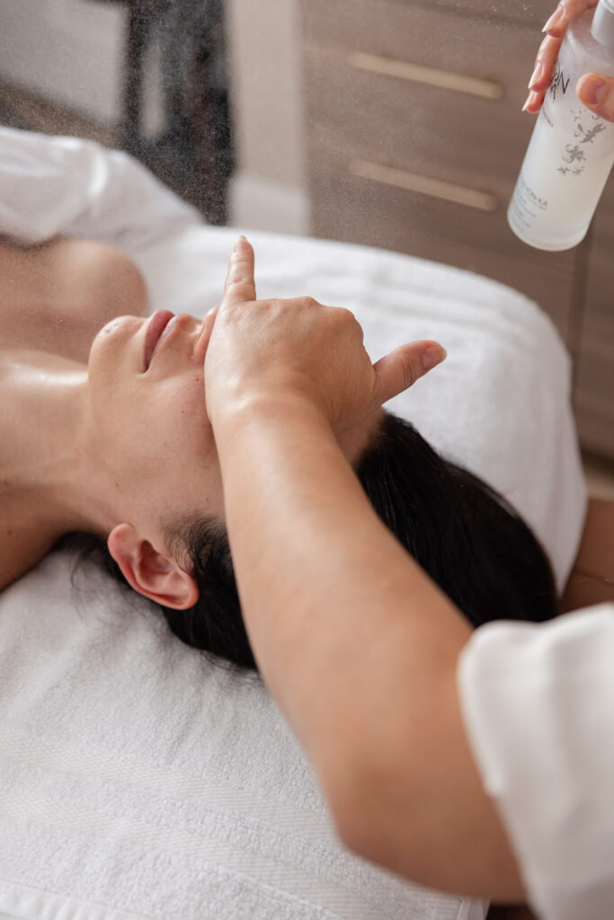 a woman lays on a massage bed and is spritzed by a luxury skincare product