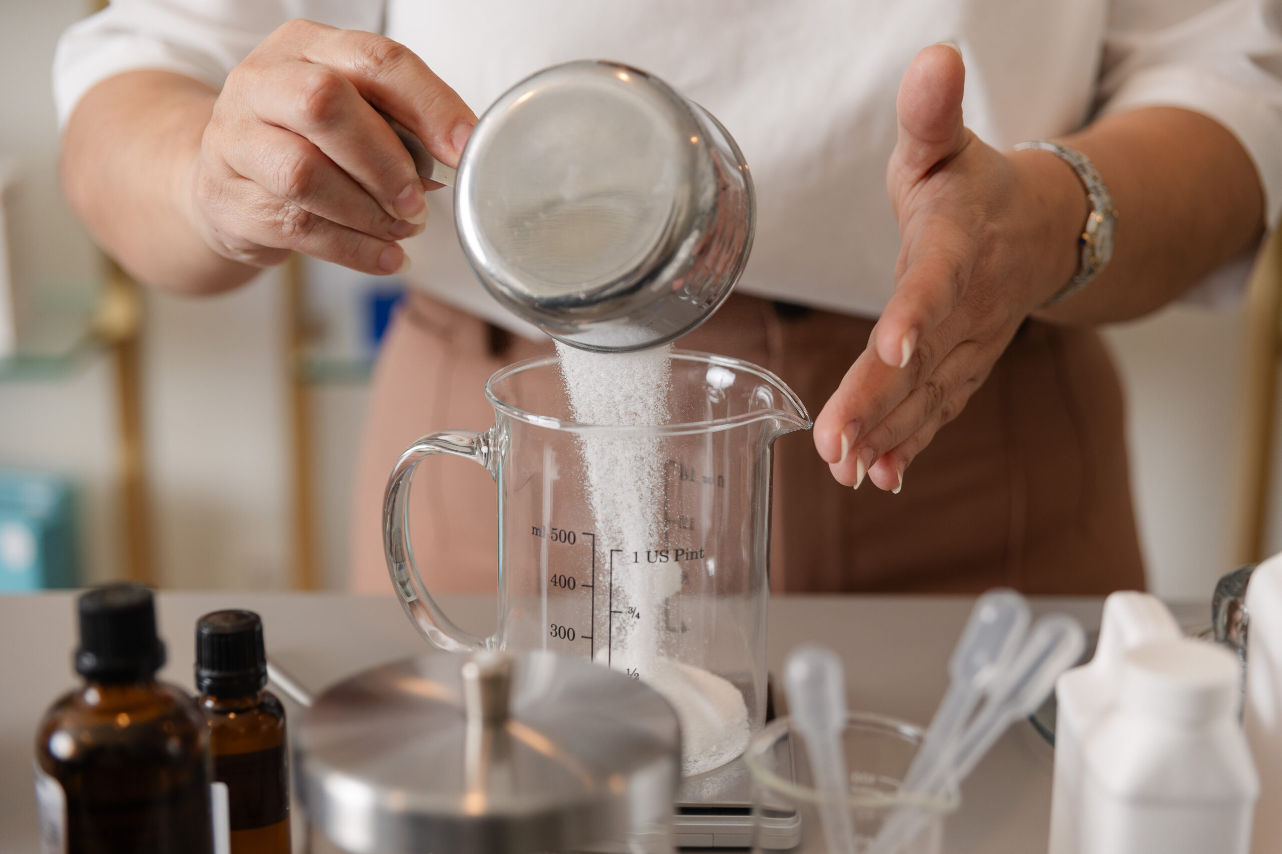 a woman pours sugar into a beaker to create a custom homemade sugar scrub
