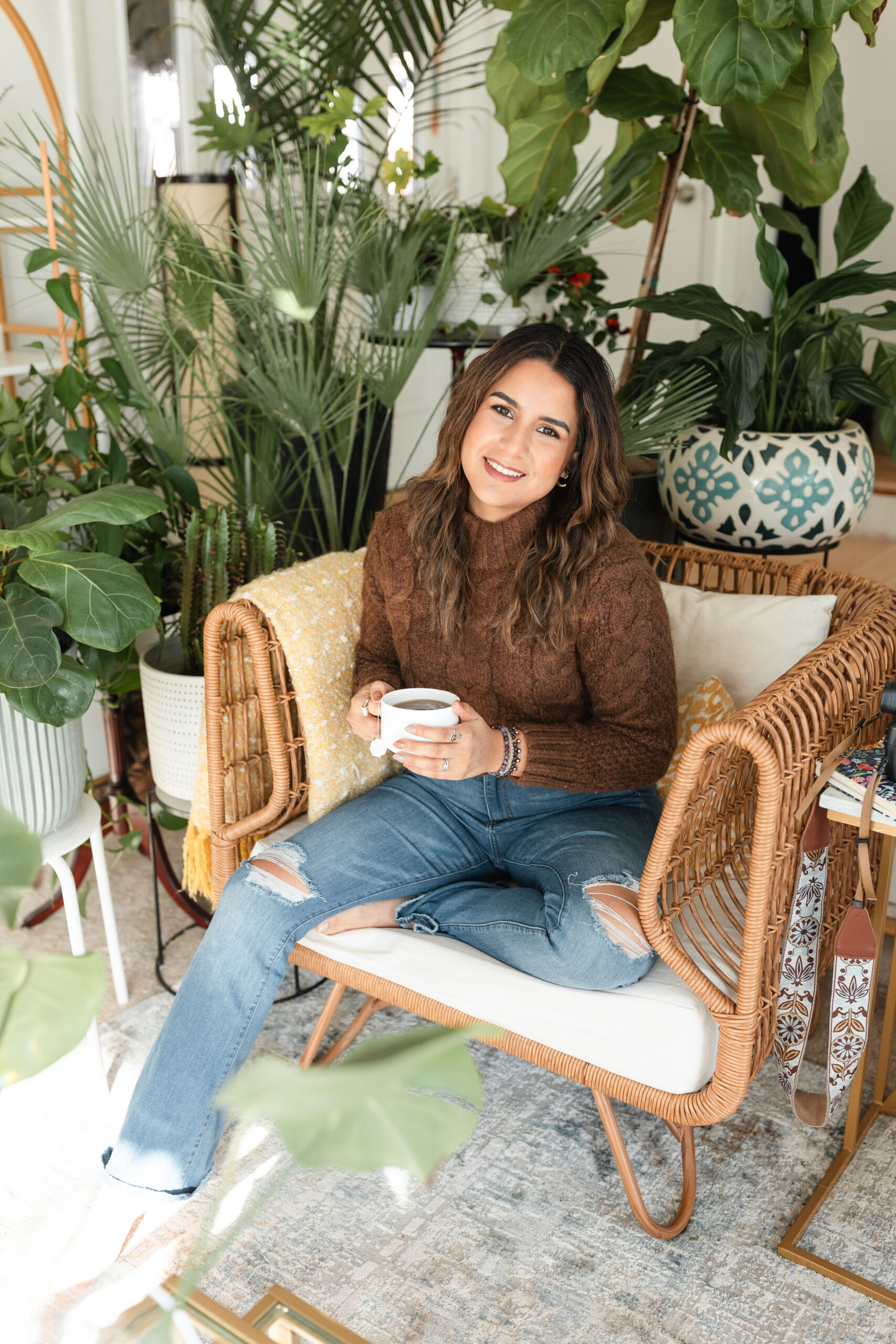 a latina photographer sits surrounded by plants holding a mug of tea