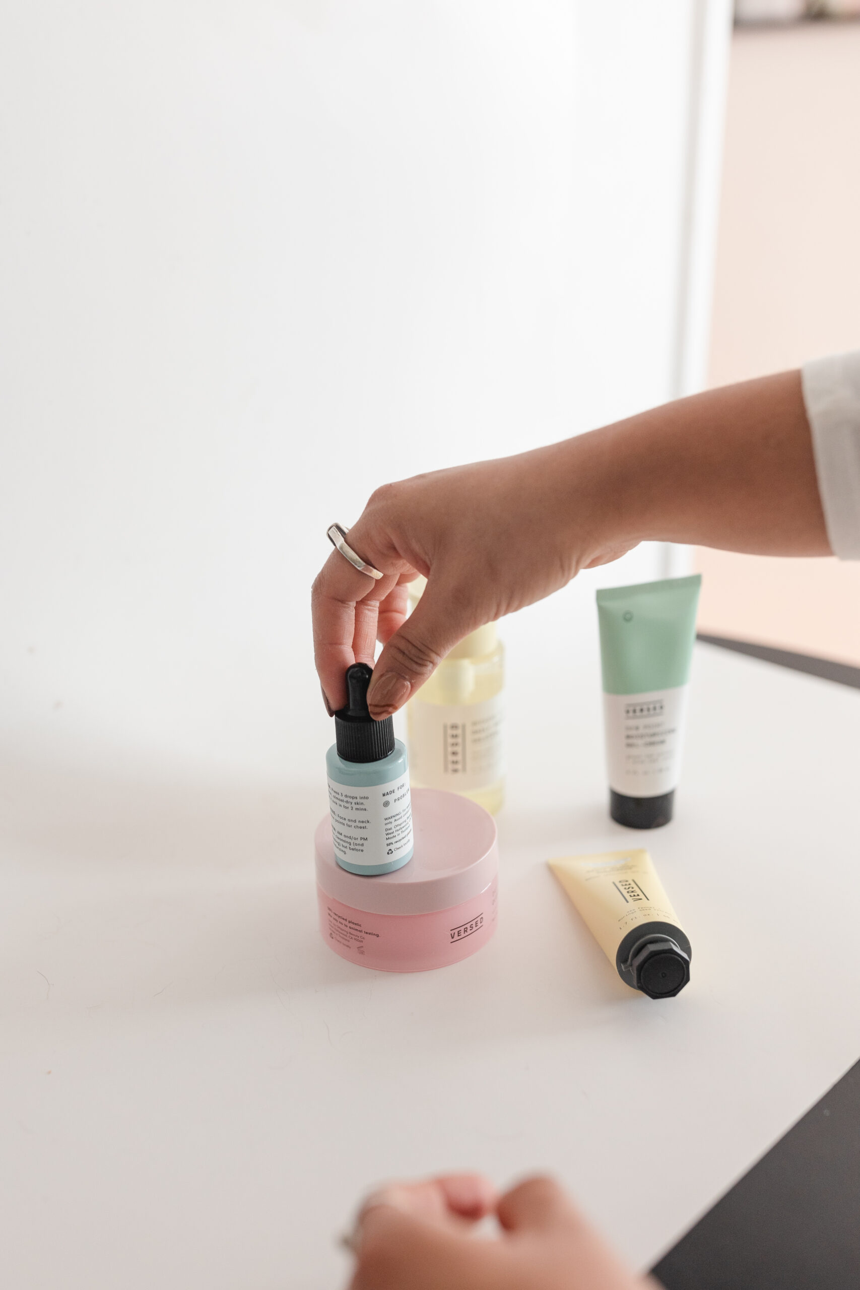 a latina photographer arranges skincare products on a white backdrop for product photography