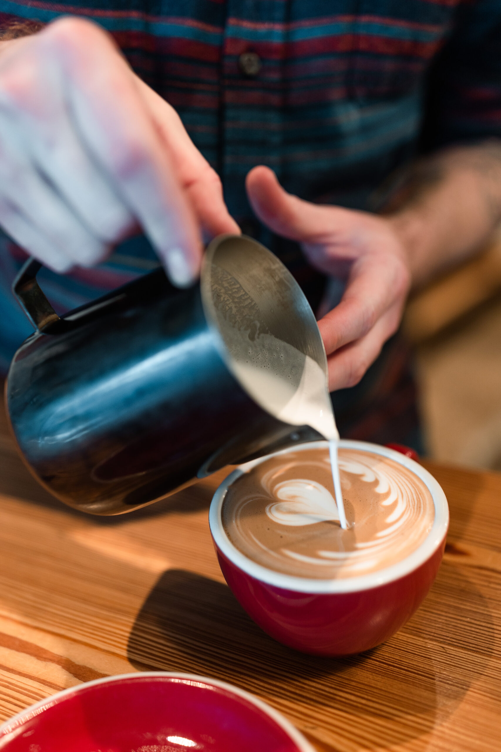 A barista at Rare Bird Coffee Roasters in Falls Church City, Virginia pours perfect latte art into a red mug