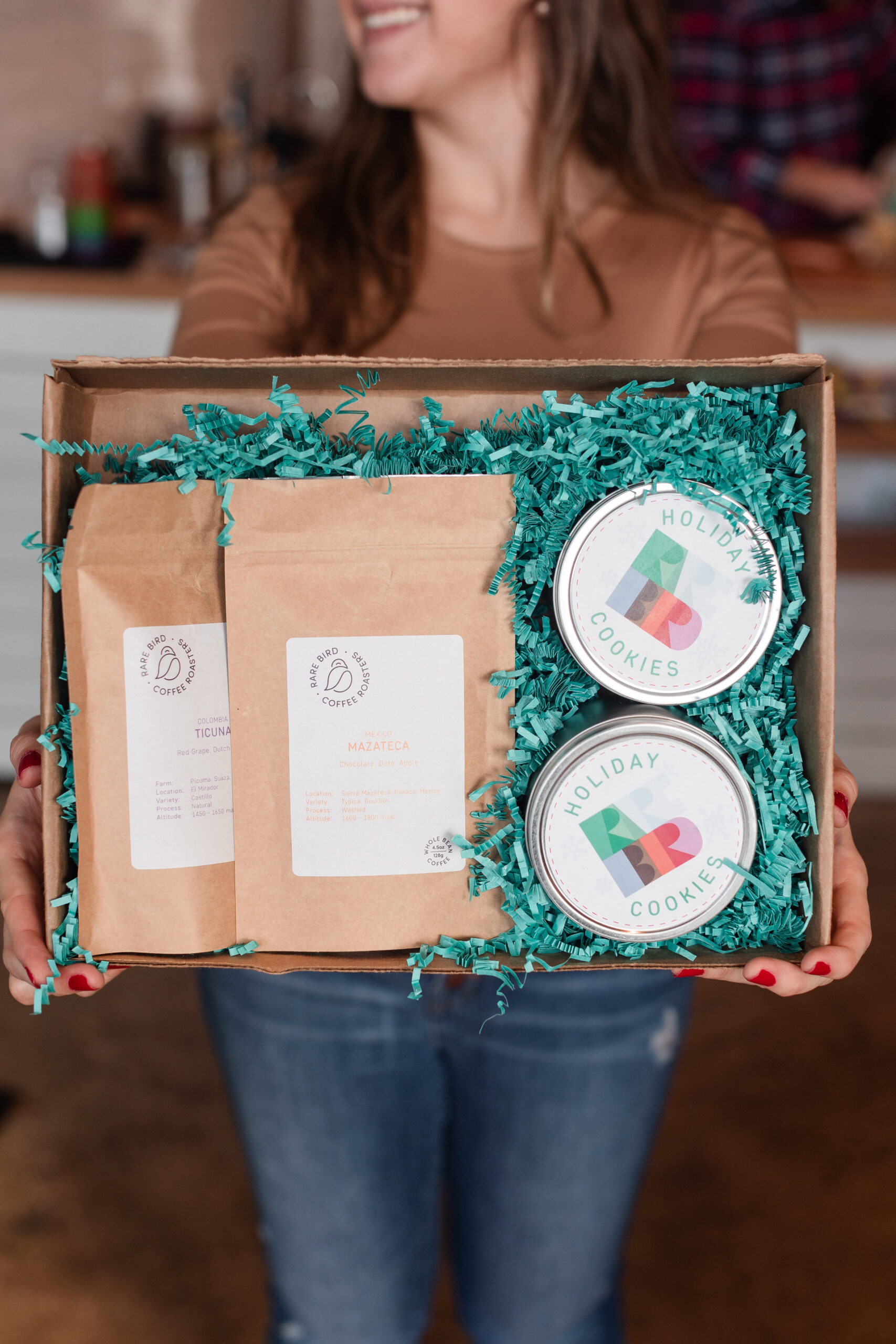 A woman holds out a holiday gift box from Rare Bird Coffee Roasters in Falls Church City, Virginia with coffee and cookies.