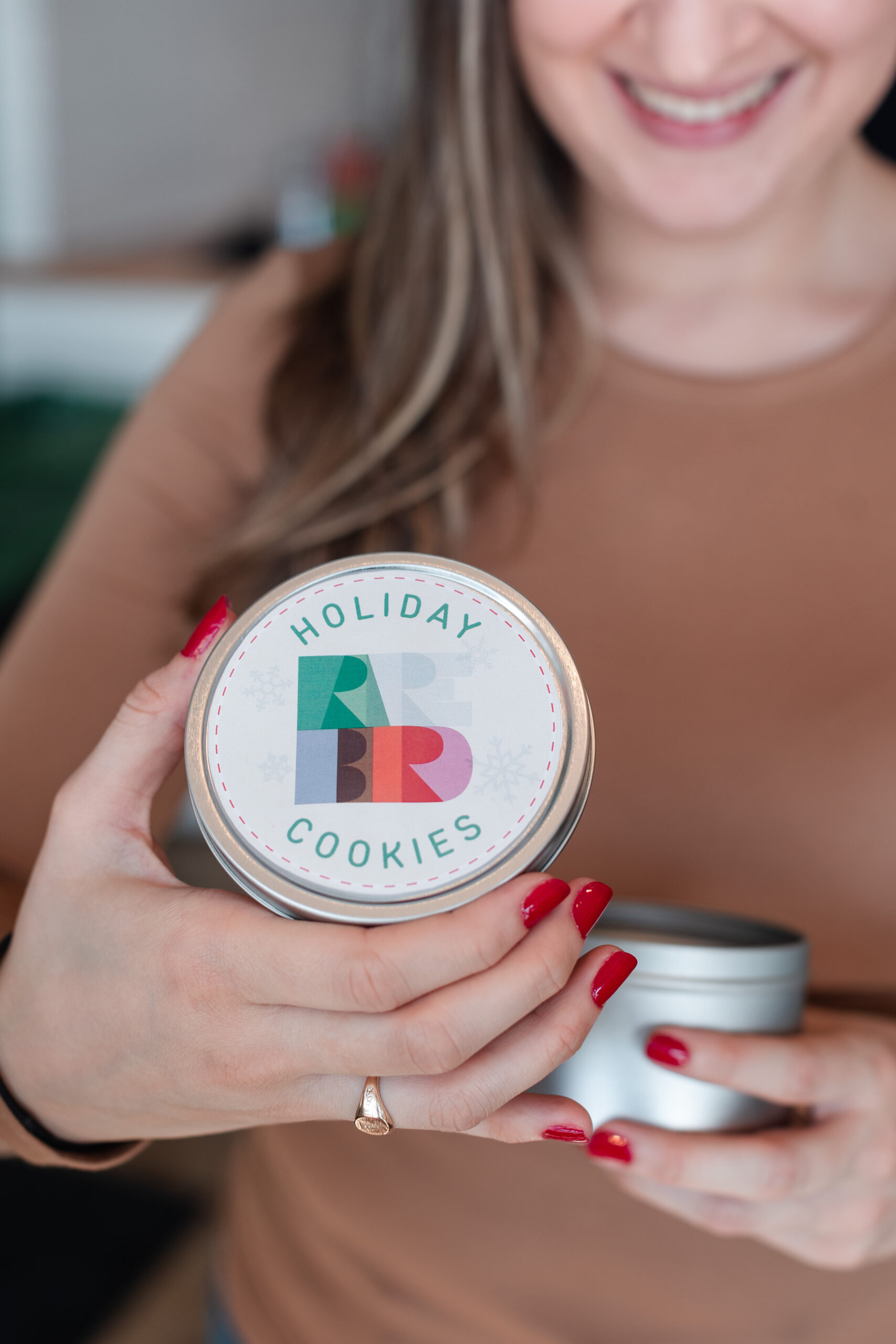 A woman smiles as she opens a holiday cookie tin from the Rare Bird holiday gift box