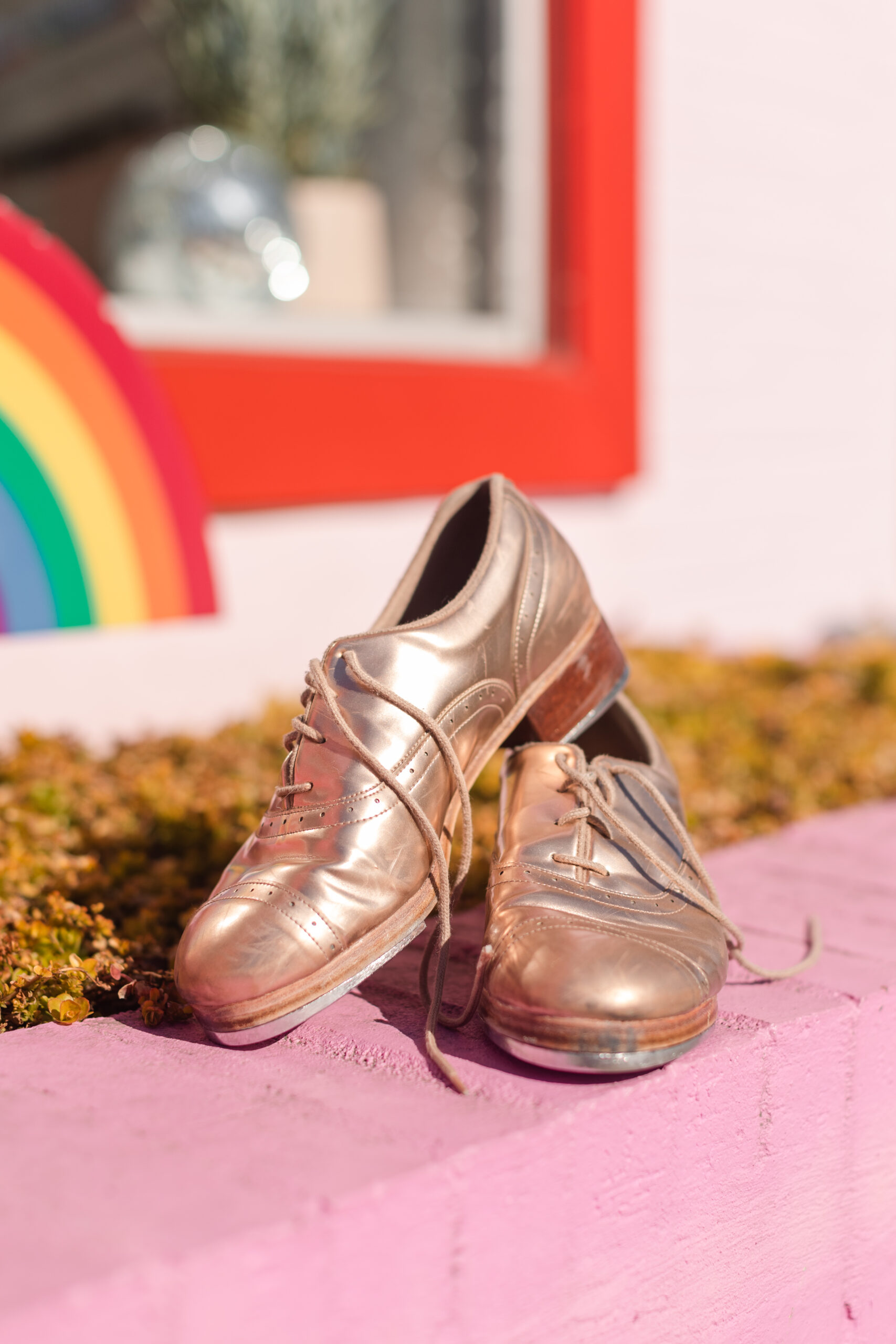 gold tap shoes displayed in front of a colorful rainbow painted wall