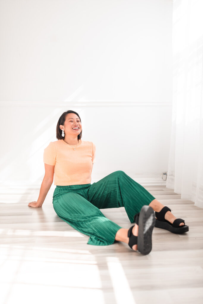 a laughing woman sits on the floor casually while leaning back on her hands