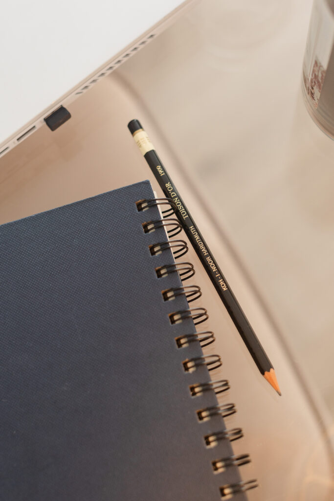 a spiral bound sketchbook and sharp pencil on a clear acrylic desktop